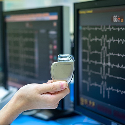 Hand holding pacemaker in front of an EKG monitor