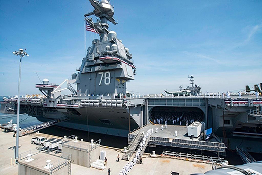 A docked Naval aircraft carrier with sailors walking on board